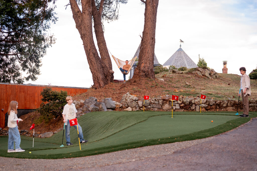 Kids playing mini golf while dad sits on hammock swing watching.