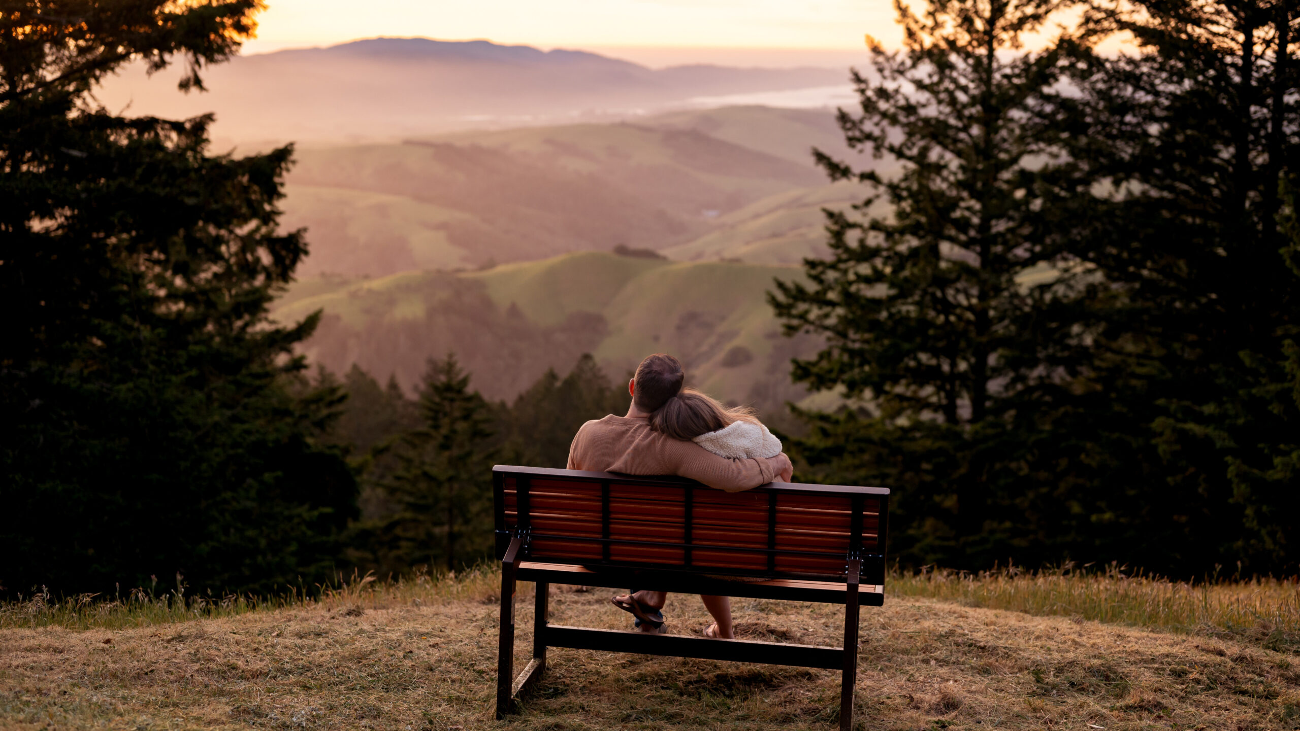 A couple sitting on a bench overlooking the sunset with Black Mountain and Tomales Bay.