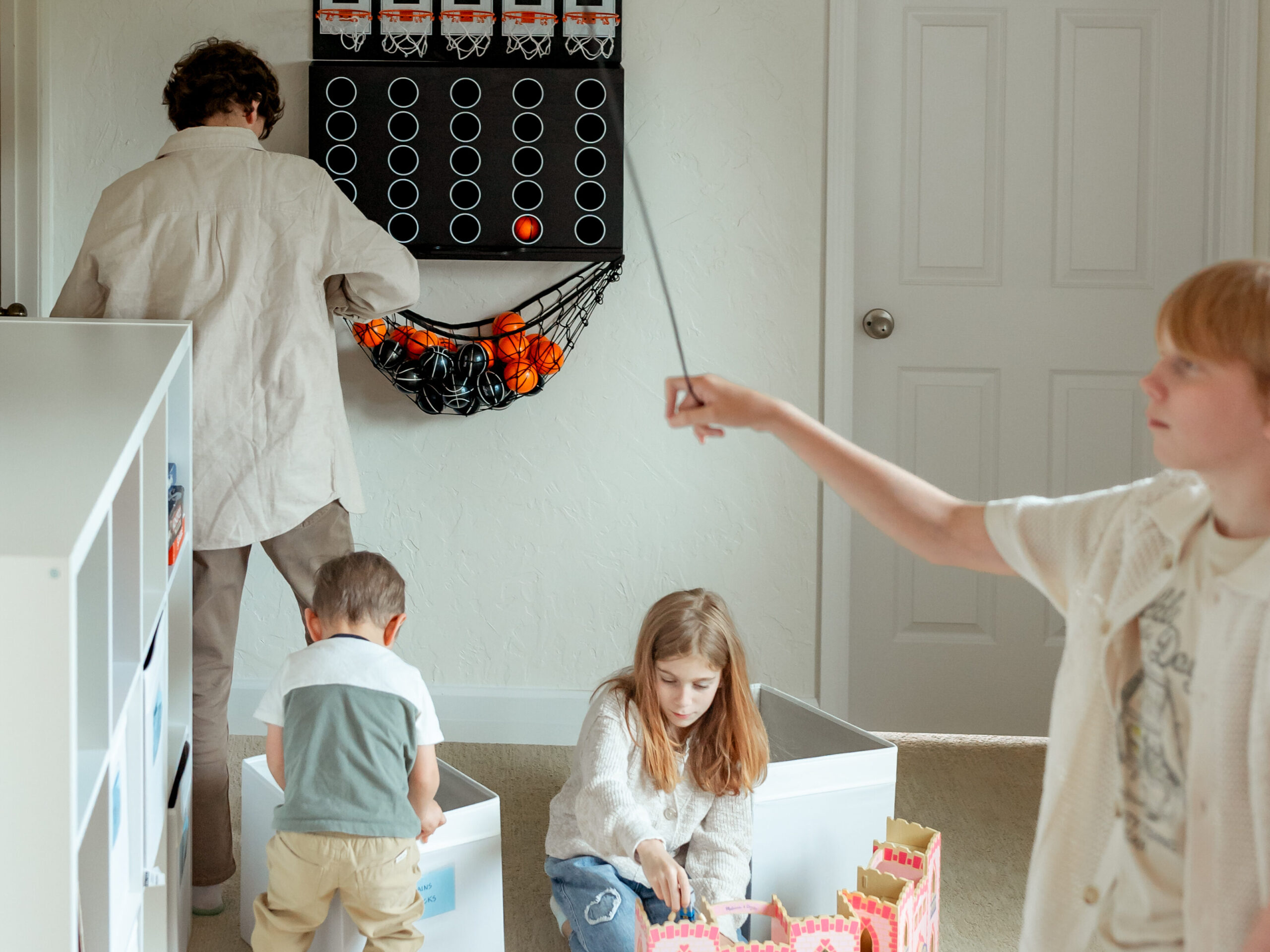 Kids in playroom, playing indoor basketball, ring hook, and castle doll house.
